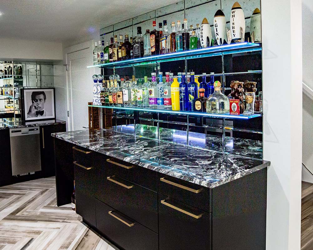 Matte black cabinets with brushed gold hardware, vintage mirror backsplash and glass shelves by Hellenbrand Glass with LED lights